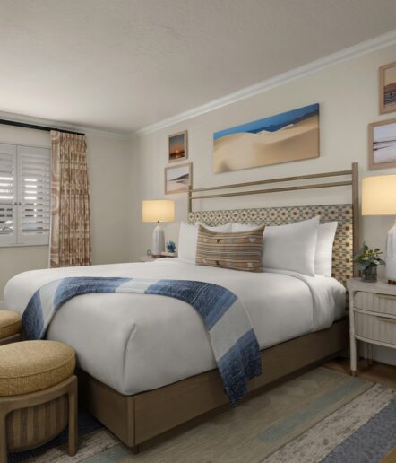 A cozy, modern bedroom with a neatly made bed featuring white linens and blue accents, two nightstands with lamps, woven stools at the foot of the bed, beach-themed wall art, and soft natural lighting.